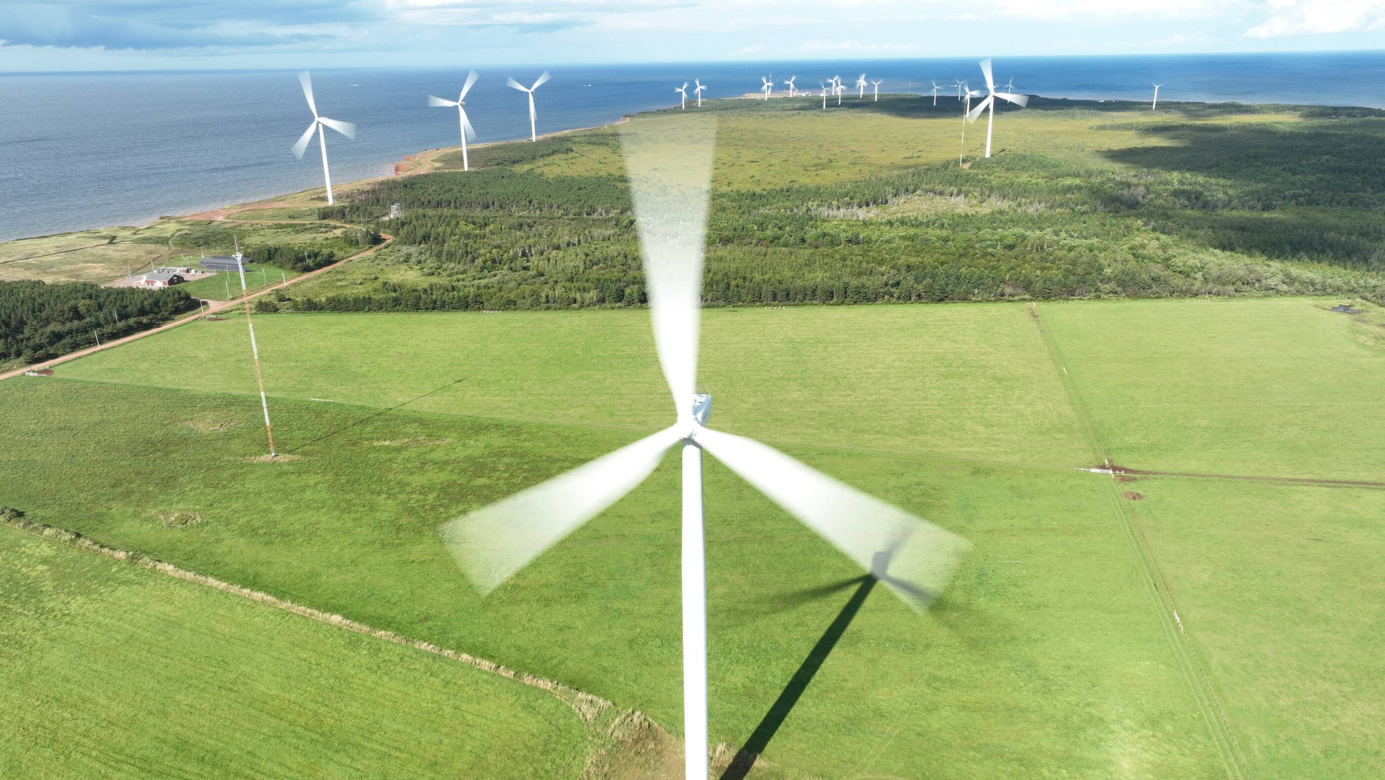 Wind farm over grassy fields next to a body of water.